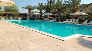 A swimming pool with lounge chairs and umbrellas, surrounded by palm trees and buildings.