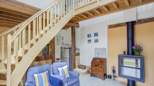 A staircase with wooden railings leading to a second floor, a blue armchair with striped pillows, a wooden chest of drawers, and a black television on a wall.