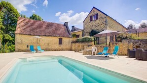 A swimming pool with lounge chairs and a stone building with a tiled roof.