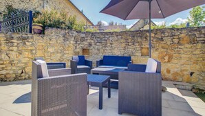 An outdoor patio with wicker furniture, a stone wall, and a large umbrella.