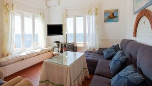 Olohuoneessa on sohva, pöytä ja televisio. Siellä on myös ikkunat, joissa on verhot, taulu ja ovi.