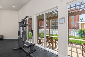 A gym with exercise equipment, large windows, and a view of a pool and outdoor seating area.