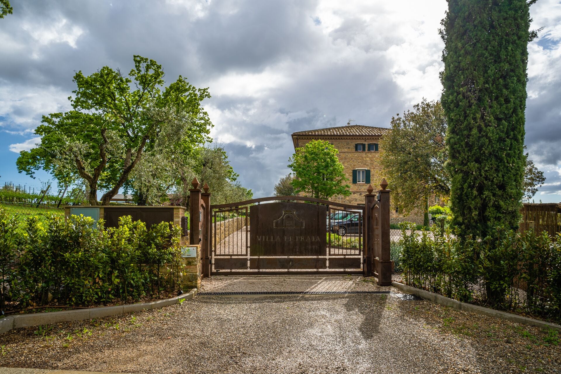 Uma entrada com portão para Villa Traia, com uma alameda de cascalho que leva a um edifício de pedra.