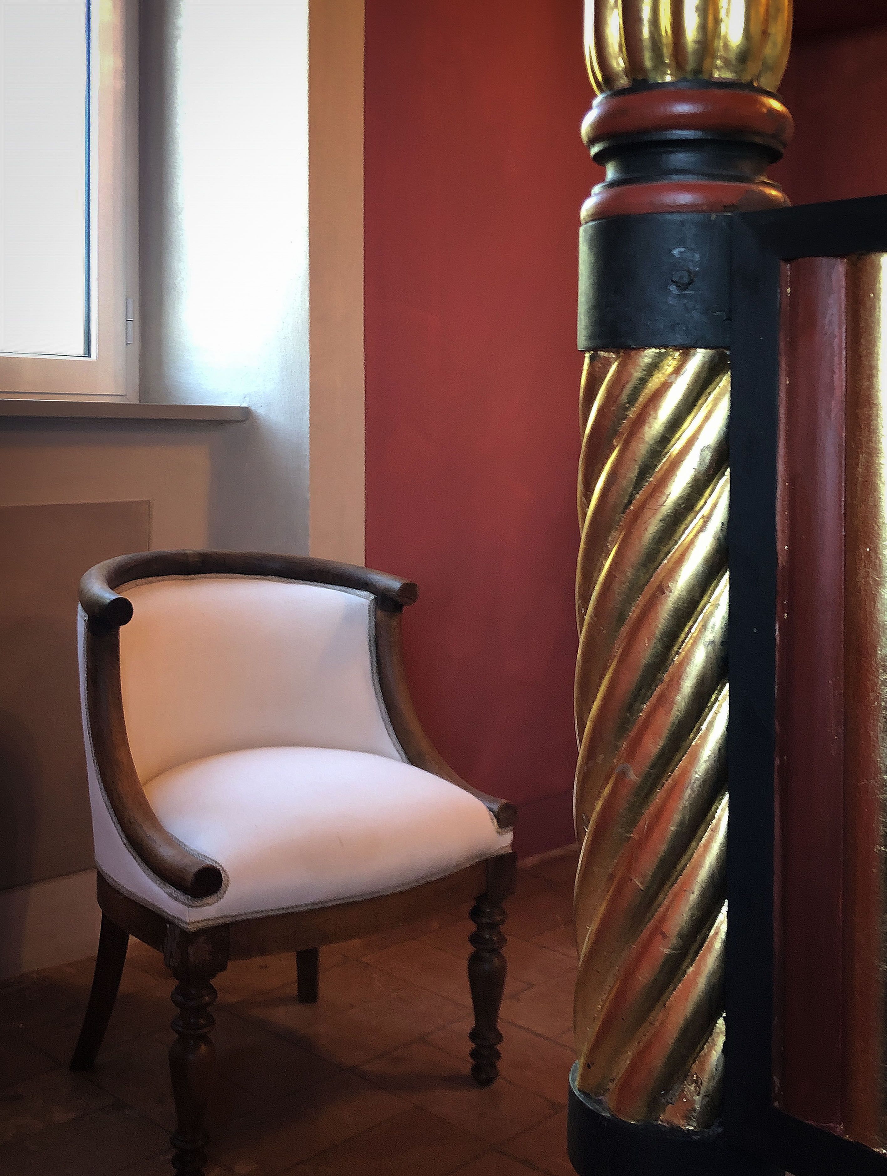 A chair with a cushioned seat and wooden legs, positioned next to a column with a twisted design.