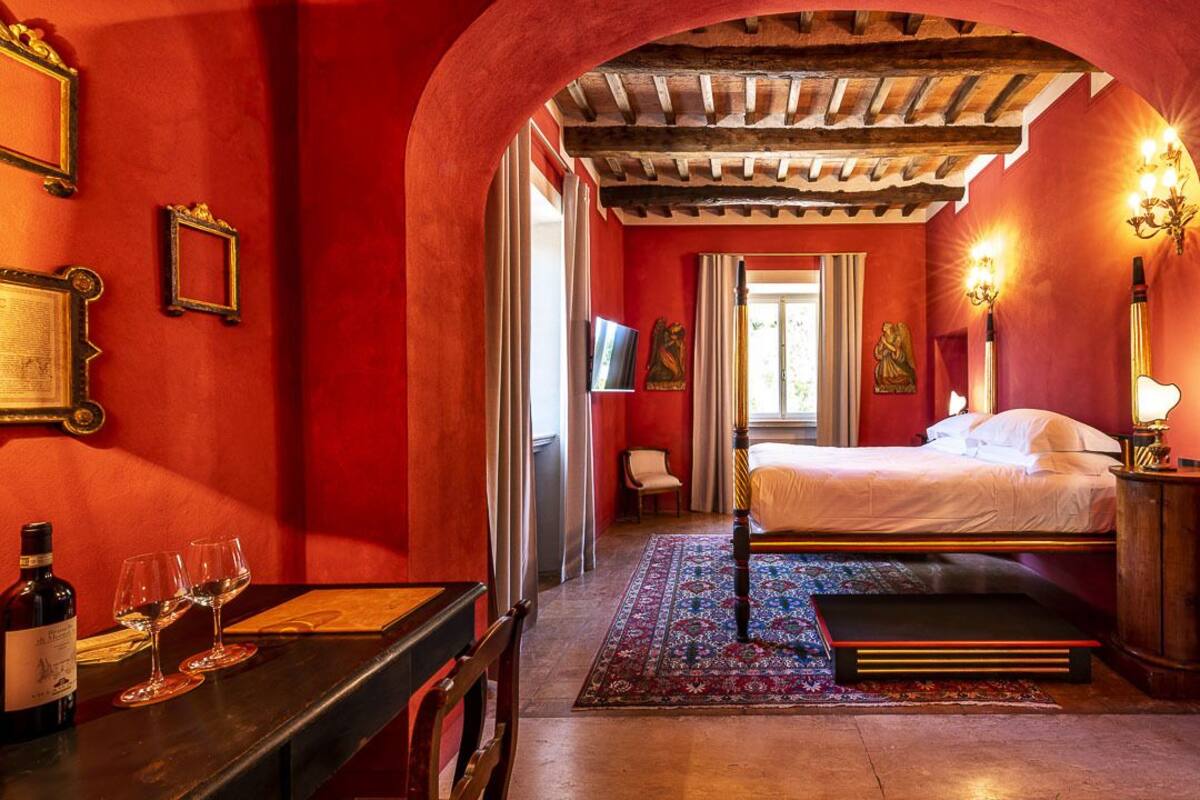A room with a bed, a table with wine glasses, and a chair.
