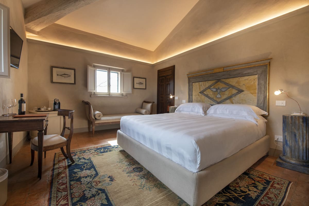 A bedroom with a large bed, a desk with a chair, a window, and a decorative headboard.