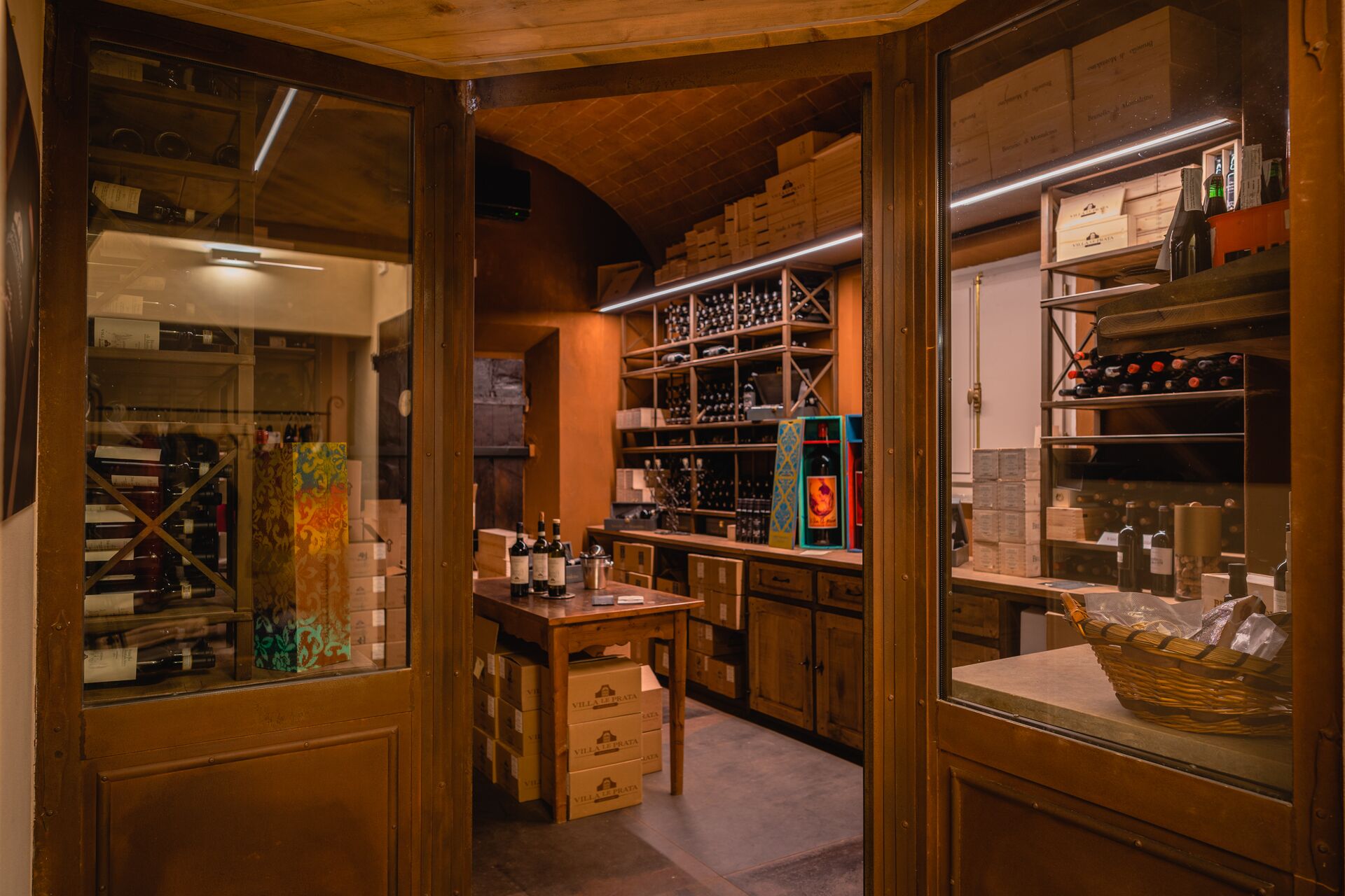 A wine cellar with wooden shelves and boxes, a counter with bottles, and a basket on a table.