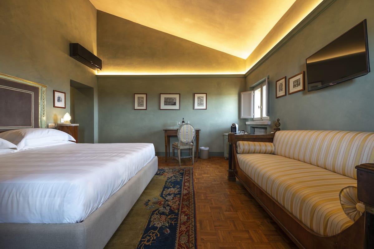 A hotel room with two beds, a sofa, a desk with a chair, a television, and framed pictures on the wall.