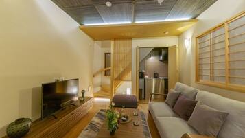 A modern living room with a flat-screen TV, wooden furniture, a sofa, and a kitchen in the background.