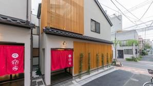 A traditional Japanese house with a modern facade, a wooden slat entrance, and a red awning with a logo.