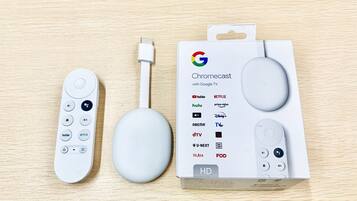 A Chromecast device, a USB cable, and its packaging on a wooden surface.