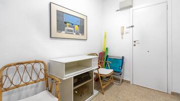 Una habitació amb una porta blanca, un quadre al mur, un armari blanc, una cadira de vimet i una cadira blava.