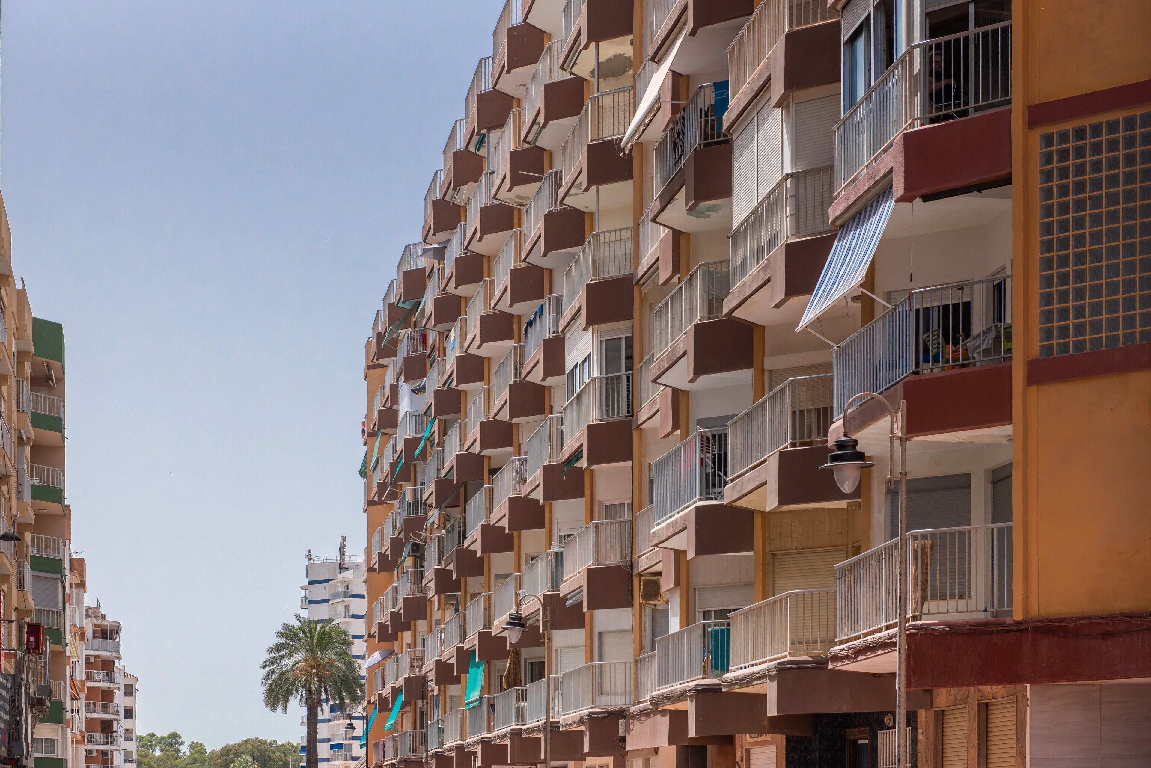 Un edifici residencial de diversos pisos amb balcons, una palmera al fons i un cel serè.