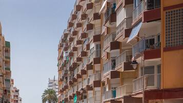Un edifici residencial de diversos pisos amb balcons, una palmera al fons i un cel serè.
