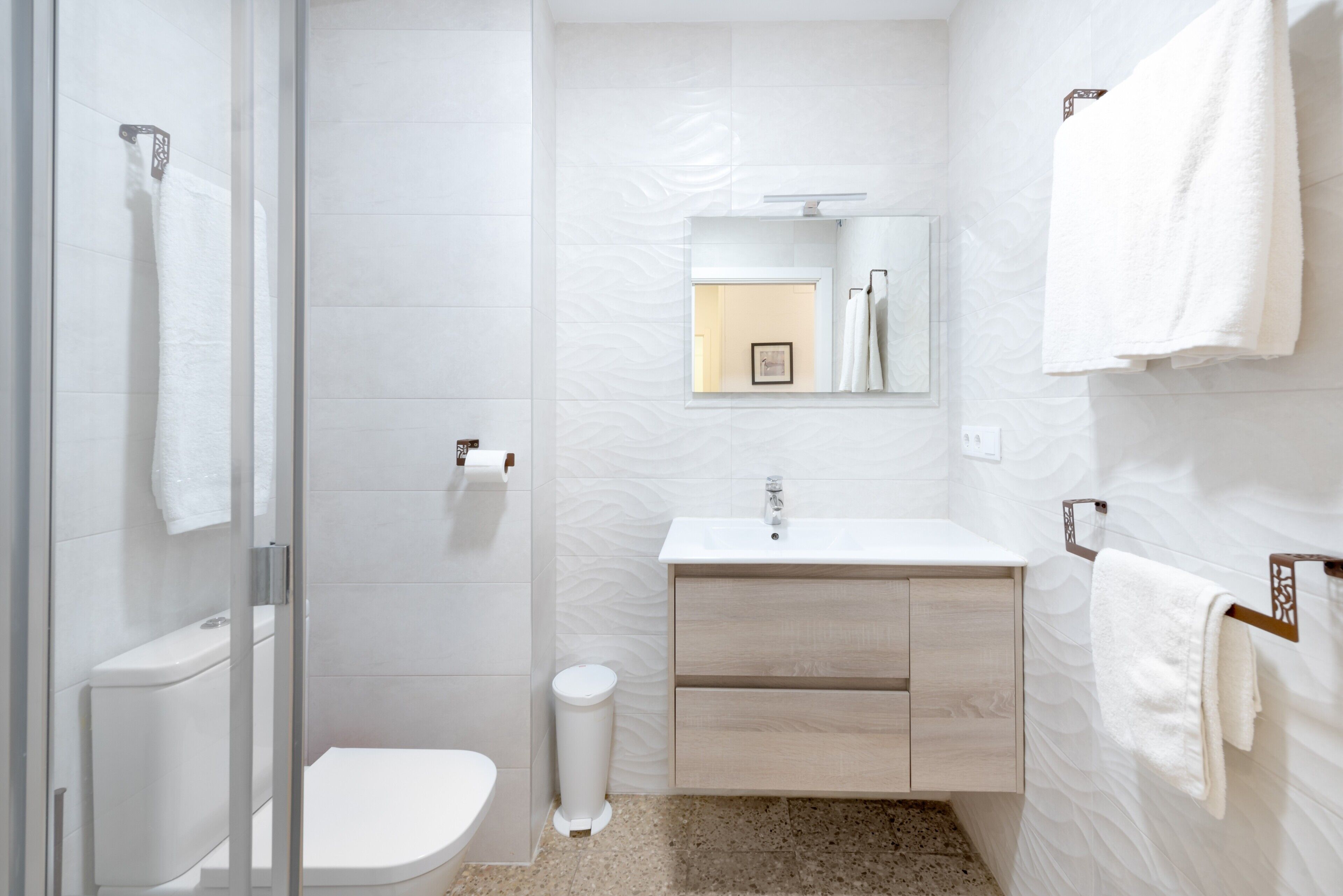 A modern bathroom with a glass shower enclosure, a white toilet, a sink with a mirror, and a towel rack.