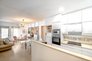 A modern kitchen with white cabinetry, a microwave, and an oven. There is a dining area with a table and chairs. - Sea Views Playa El Perelló Valencia (Sueca)