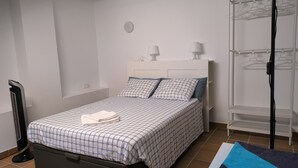 Ein ordentlich bezogenes Bett mit einem gemusterten Überwurf, einer Nachttischlampe und einem an der Wand befestigten Regal.