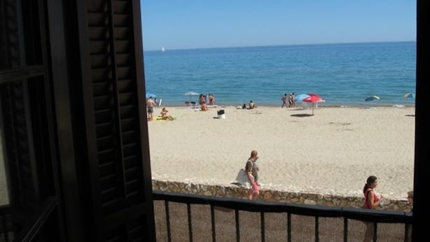 Blick auf einen Strand von einem Balkon mit einer Steinmauer und einem Metallgeländer.