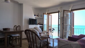 Ein Zimmer mit Balkon, Fernseher, Esstisch und Stühlen.