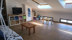 A room with a TV, a table, a chair, a bookshelf, and a skylight. - Baywatch Penthouse with Sea Views, Balcony and Wi-Fi (Altafulla)