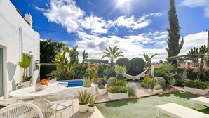 A patio with a white table and chairs, a small pool, and various potted plants.