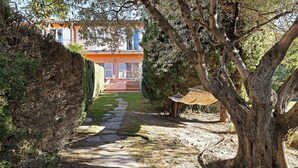 Un chemin menant à un bâtiment à la façade rouge, entouré d’arbres et agrémenté d’un hamac.