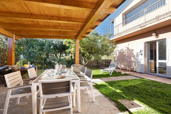 Une terrasse extérieure dotée d’une pergola en bois, d’une table avec des chaises et d’une pelouse.