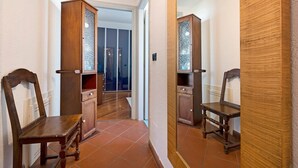Un couloir meublé de meubles en bois, avec un miroir et une porte donnant sur une pièce dont le sol est recouvert de carreaux.