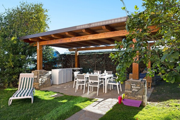 Un patio couvert avec une cheminée en pierre, une table à manger avec des chaises et un fauteuil de relaxation.