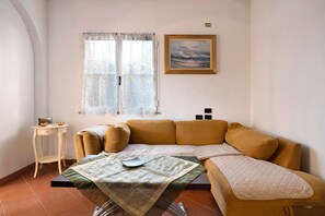 Une pièce confortable avec un canapé, une petite table, une fenêtre avec des rideaux et un tableau au mur.