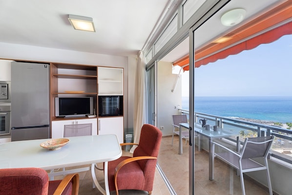 Un balcon avec vue sur l’océan, un coin repas avec une table et des chaises, et une kitchenette équipée d’un réfrigérateur et d’un four à micro-ondes.