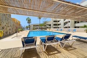 Un espace piscine avec des chaises longues et une zone abritée.