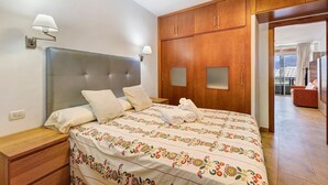 Een slaapkamer met een bed, nachtkastjes, een houten garderobe en uitzicht op een balkon.