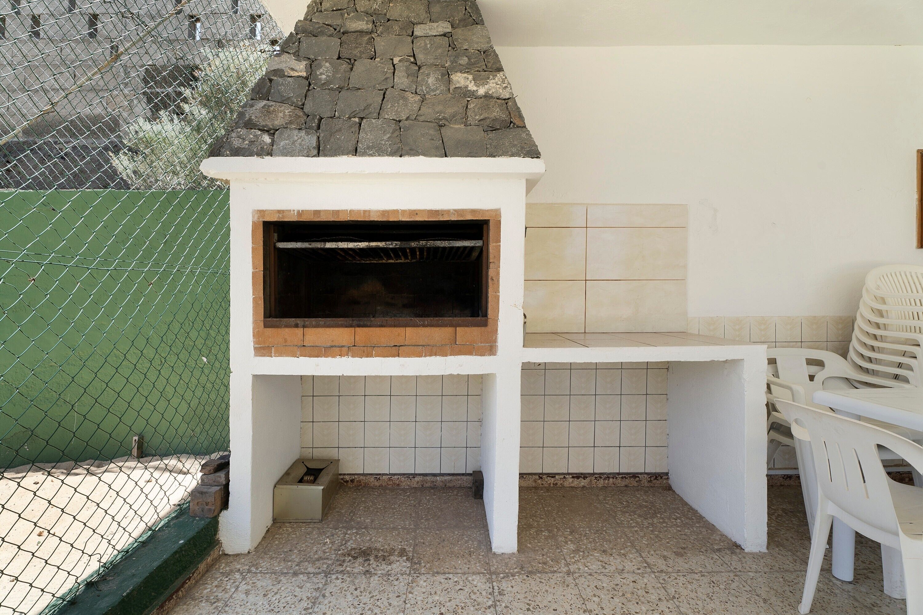 Ein Grill mit Steindach, einer Fliesenwand und einem weißen Tisch mit Stühlen.