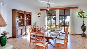 A dining room with a marble floor, wooden chairs, a long table set for six, and a large window with a view. - Villa 'Albuar' with Sea View, Pool, Garden & Wi-Fi (São Rafael)