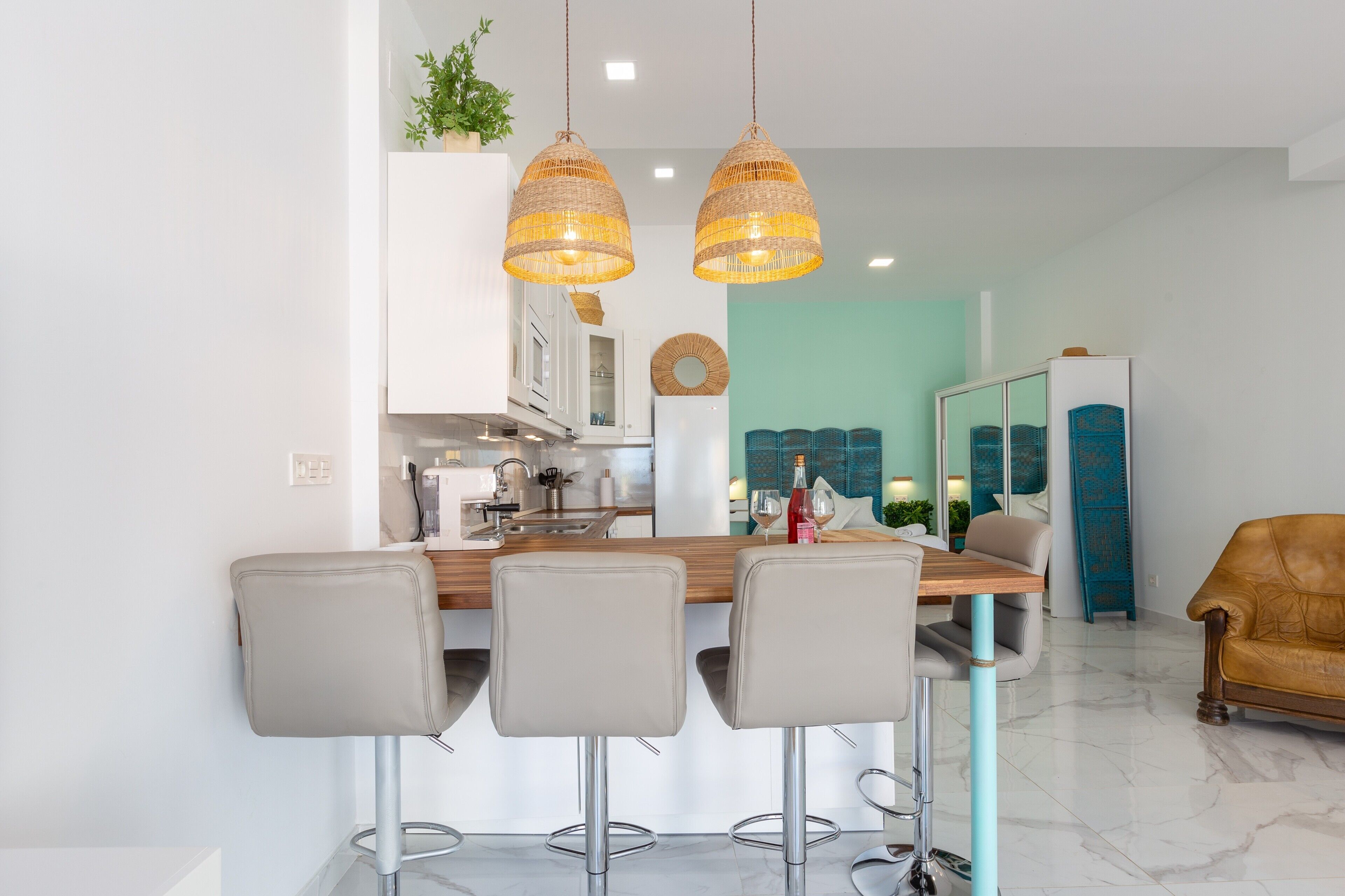 A modern kitchen with white cabinets, a wooden island with bar stools, and hanging wicker pendant lights.