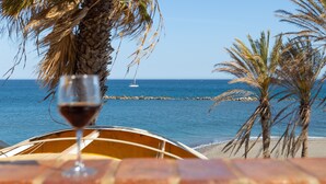 Strandudsigt med et glas rødvin, palmer og en båd på vandet.