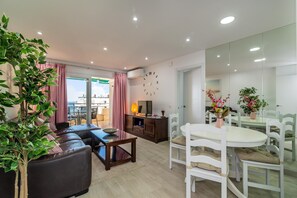 Una sala de estar moderna con sofá, mesa de comedor y sillas, televisor y un amplio ventanal con cortinas.