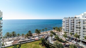 Un hotel frente al mar, con vista al océano, palmeras y un estacionamiento.
