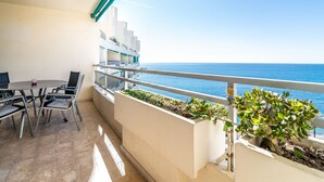 Un balcón con vista al mar, una mesa de comedor con sillas y una barandilla.
