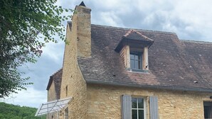 A stone house with a sloped roof, a small front door, and a window with shutters. - Authentic stone house in a typical village at the foot of a castle! (Berbiguières)