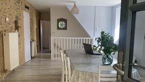 A spacious dining area with a round table, white chairs, and a hanging light fixture. - Authentic stone house in a typical village at the foot of a castle! (Berbiguières)