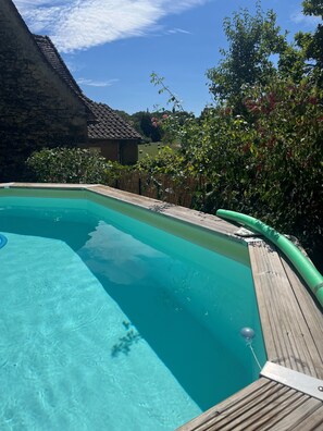 Une piscine d’un bleu éclatant, dotée d’une terrasse en bois et d’un tuyau d’arrosage vert.