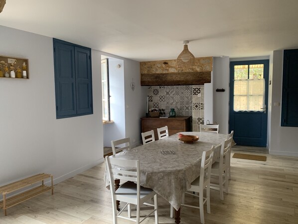 Un espace repas comprenant une table ronde, des chaises blanches et un banc en bois.