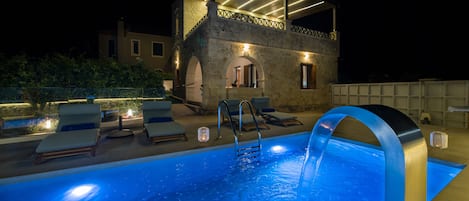 A swimming pool with lounge chairs and a stone building with a covered patio area.