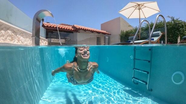 Ein Hallenbad mit klarem Wasser, einer Leiter und einer Liege mit Sonnenschirm.