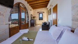 Ein Schlafzimmer mit Bett, Holzboden, Steinwänden, Fernseher, Schreibtisch und Blick auf die Landschaft.