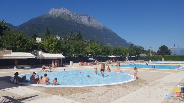 A swimming pool area with multiple pools, surrounded by trees and a mountain in the background.