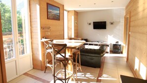 A spacious room with a wooden interior, a dining area with chairs and a table, a sofa, and a television mounted on the wall.