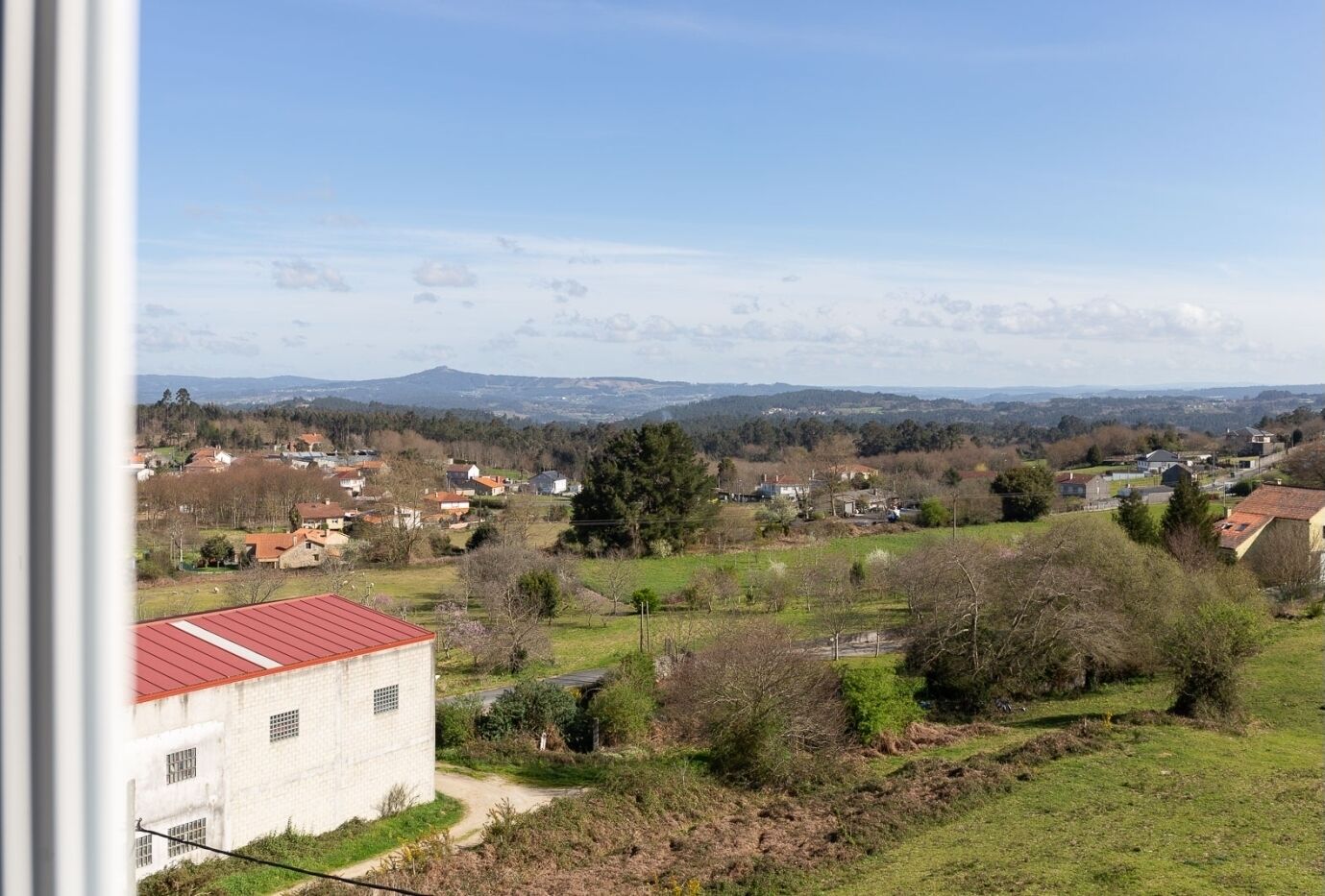 A rural landscape with houses, trees, and a distant mountain range.